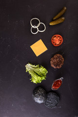 Ingredients for cooking black burger. Grilled chicken patty, buns, onion, tomatoes, lettuce, pickles, sauce, cheese over black background, top view