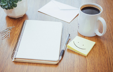 notepad and pen beside a cup of coffee on a wooden table outdoors at a cafe.