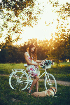 Young Woman And Dog With A Bike In The Park On Sunset