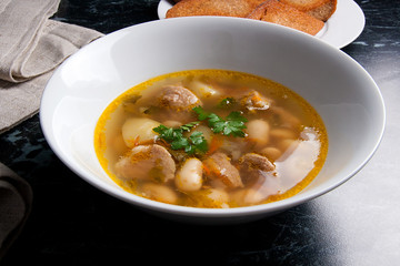 Bean soup in white plate, several toast on white plate on a black stone background.
