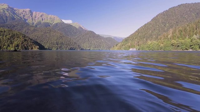 Beautiful tranquil landscape of the lake Ritz in Abkhazia, sunny weather, light and water ripple summer mood, people float down the river, a paradise for tourists