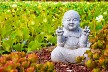 A smiling Buddha statue surrounded by lotus leaves