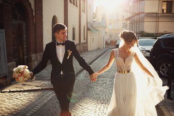 Dancing wedding couple walks in the rays of evening sun along stone street