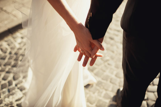 Close-up of newlyweds hands held together in the lights of evening sun