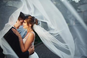 Wind blows veil on bride and groom looking at each other with love