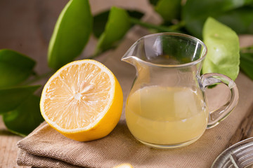 glass bowl of freshly squeezed lemon juice, lemon squeezer and ripe lemons on wooden background