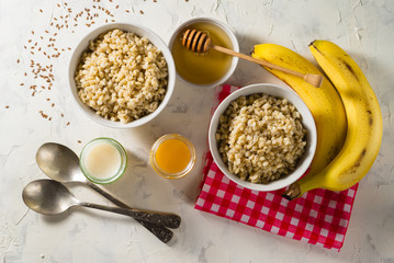 Healthy breakfast. Light background with red napkin. Barley porridge, flax seeds, bananas, soy milk, peach juice and honey.