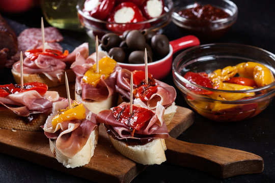 Spanish tapas with slices jamon serrano and grilled pepper. Also olives, salami, pickled onions, and peppers stuffed with cheese