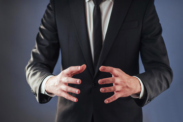Obraz premium The young businessman in a suit shows his hand on a dark background isolated