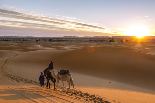 Tuareg man with camels and tourists at the Erg Chebbi sand dunes, Sahara Desert, Merzouga, Morocco.