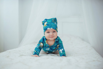 Newborn baby dressed in a green suit lying on a soft bed in a white studio.