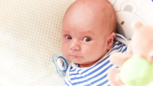 Top view shot of cute baby with soother lying in crib and looking at spinning taddy bear toys