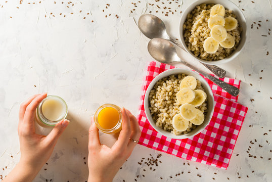 Healthy breakfast. Light background with red napkin. Barley porridge, flax seeds, bananas, soy milk, peach juice. Hands.