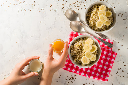 Healthy breakfast. Light background with red napkin. Barley porridge, flax seeds, bananas, soy milk, peach juice. Hands.