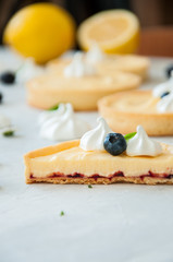 Cut of lemon curd and blueberry jam tarts with meringue and basil leaves chamomiles whole and slices of fresh lemon on a white stone background. Copy Space. Flat lay. Top View.