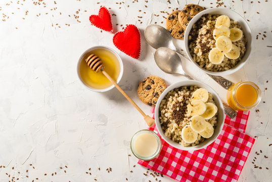 Healthy breakfast. Light background with red napkin. Barley porridge, flax seeds, bananas, soy milk, peach juice, cookies with chocolate chips and honey. Two hearts.