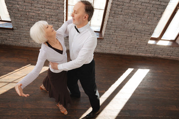 Cheerful aged couple waltzing at the ballroom