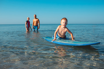 Surfers and their son are going to surf in the ocean in a sunny day