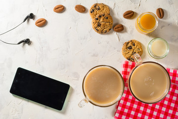 Obraz na płótnie Canvas Healthy breakfast. Light background with red napkin. Coffee, soy milk, peach juice and cookies with chocolate chips. Mobile phone and headphones.