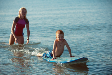 Young woman teaching surfing her son in the ocean in a sunny day