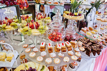 Wedding reception table with different fruits, cakes and sweets.