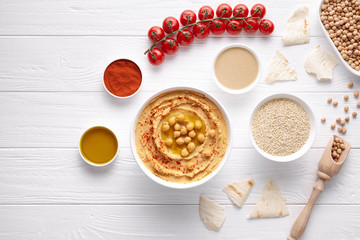 Bowl of hummus traditional arab healthy vegan dip chickpeas paste snack flat lay with natural ingridients, tahini, paprika, olive oil, pitta on table. Healthy vegetarian diet nutrition protein food