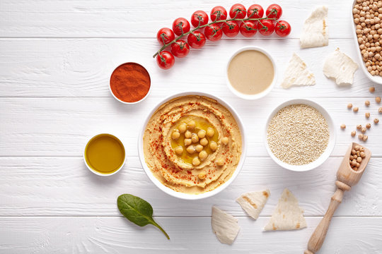 Bowl of hummus mediterranean healthy vegan dip chickpeas paste snack flat lay with natural ingridients, tahini, paprika, olive oil, pitta on table. Healthy vegetarian diet nutrition protein food