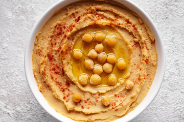 Hummus homemade middle eastern dip paste close up with paprika, tahini, and olive oil, healthy diet natural vegetarian snack protein food. Traditional mediterranean appetizer on white table