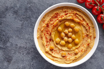 Hummus homemade middle eastern dip paste close up with paprika, tahini, sesame, and olive oil, healthy diet natural vegetarian snack protein food. Traditional mediterranean appetizer on blue table