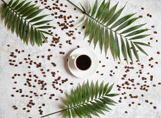 Cup of black espresso on a white creative concrete background with coffee beans and palm branches. Rest in warm tropical countries concept. Flat lay drink composition.