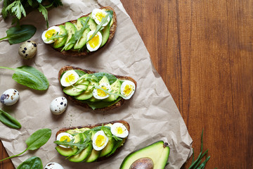 Sandwiches of whole wheat bread with avocado, spinach, guacamole, arugula and quail eggs on parchment. Healthy breakfast or lunch concept. Flat lay composition with copy space.