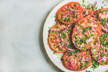 Fresh heirloom tomato, parsley and onion salad in white plate over light grey marble background, top view, copy space. Clean eating, vegan, vegetarian, healthy, dieting food concept