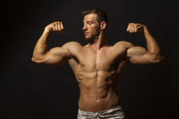 half-naked handsome and muscular young man posing on a dark background