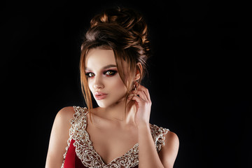 Beautiful, sexy brunette girl with big lips, hair and makeup in a long burgundy dress with precious stones. In a staged on a gray background, a place for advertising