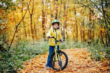 A boy is riding a bicycle in an autumn forest.