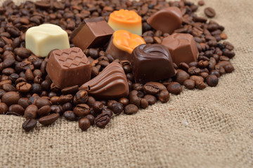 Jute background. Assortment of dark, white and milk chocolate stack on roasted  coffee beans. Sweet and rustic image. Selective macro focus. Chocolates background. Sweets