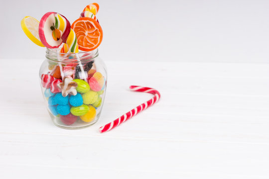 Tasty chewing sweets, lollipops and jelly candies in the glass can near candy cane