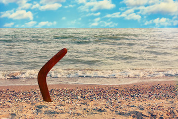 Australian Boomerang on sandy coastline against sea wave and sky.Toned image.