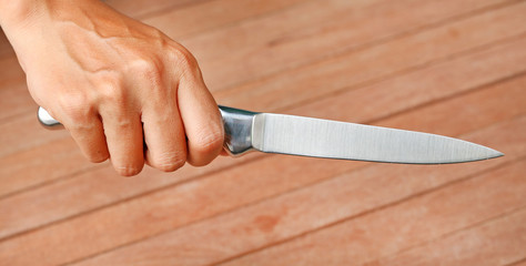 A knife being held by hands against plank wood