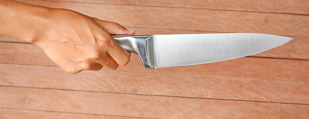 A knife being held by hands against plank wood