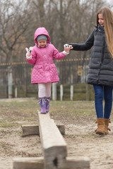 Mom leads daughter by hand through an obstacle.