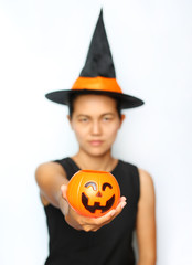 Young woman in witches hat and costume holding Jack pumpkin on a white background. Blur of Halloween Witch focus at Pumpkin.