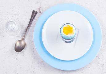 blue easter egg with yellow yolk, spoon, top view on wooden aged table - easter breakfast concept