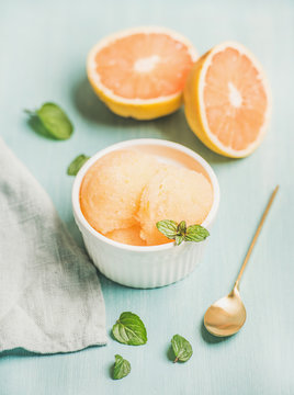 Pink grapefruit sorbet with fresh mint in white bowl over blue painted background, selective focus. Fresh healthy raw vegan summer dessert concept