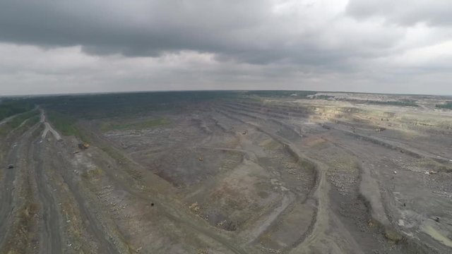 Video footage taken from a height over a giant quarry. Flight over a deep crater. The production of useful types of heavy vehicles. Excavations in the bowels of the earth. Storm clouds and giant bat.
