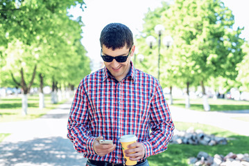 The man in the summer in the park, reading a message on your phone, glasses, watching the map and news feed  social networks, happy smiles   video film in jeans bright sunny day. Idea concept business