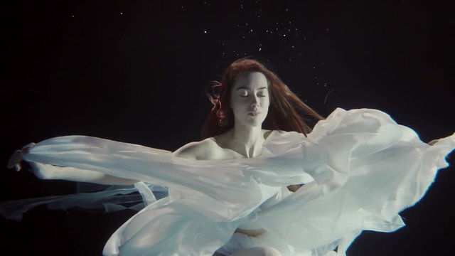 young woman swimming underwater in a white dress like a fairy tale