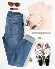 Stylish woman look. Woman/girl outfit on white background. Blue denim jeans , peach tshirt, flower print sneakers, hand watch, headphones and retro sunglasses. Flat lay, top view