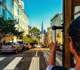 Ride with the cable car in San Francisco. Picture shows a person riding the famous MUNI train on Powell-Mason line down the hill to the bay with the famous landmark of Transamerica Pyramid in front.