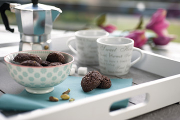 rustic biscuits cocoa and pistachios on wooden tray with coffee pot, cups, fresh pistachios, sugar cubes and flowers in the background